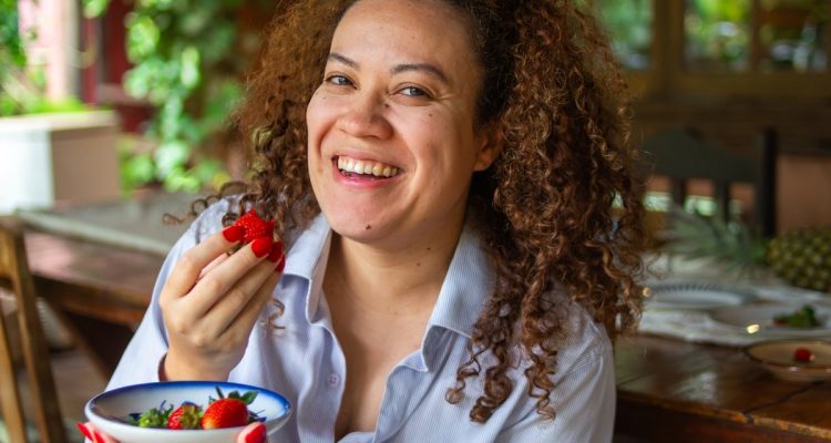 Smiling woman eating strawberries in a cozy restaurant with natural light and a warm lifestyle atmosphere.