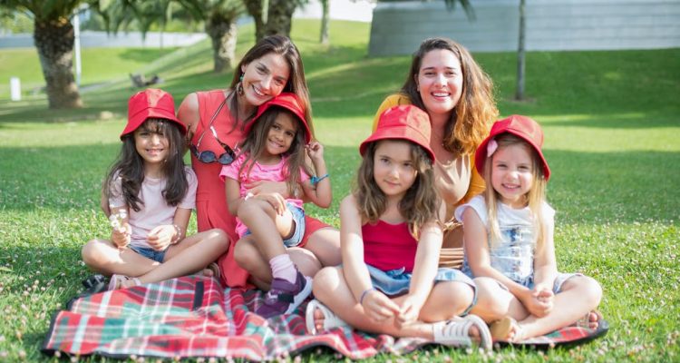 Friends enjoying a sunny day picnic on grass with bucket hats and smiles in a Portuguese park.