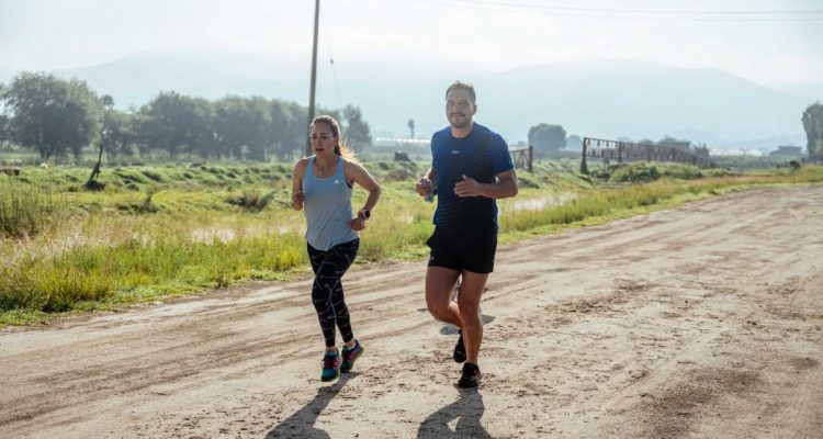 Active couple jogging on a dirt road in a scenic rural area under the bright sun.